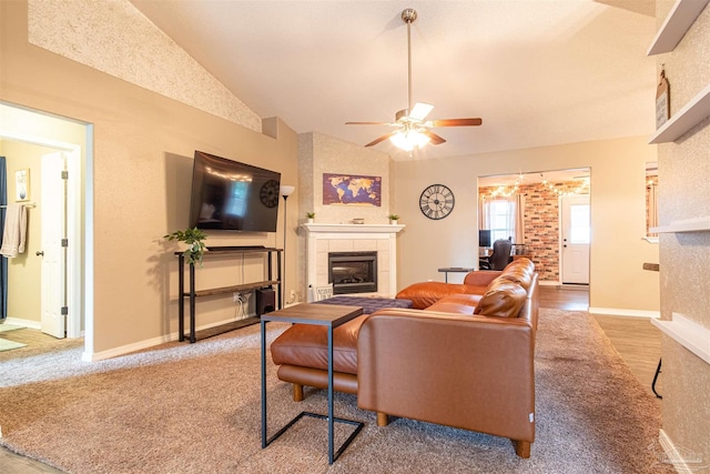 carpeted living room featuring lofted ceiling, ceiling fan, a tiled fireplace, and baseboards