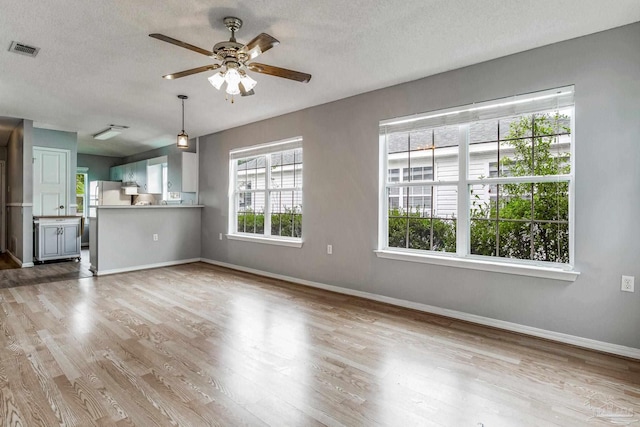 unfurnished living room featuring ceiling fan, light wood-type flooring, and a textured ceiling