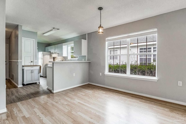 kitchen featuring white cabinets, light hardwood / wood-style floors, a textured ceiling, white fridge, and kitchen peninsula