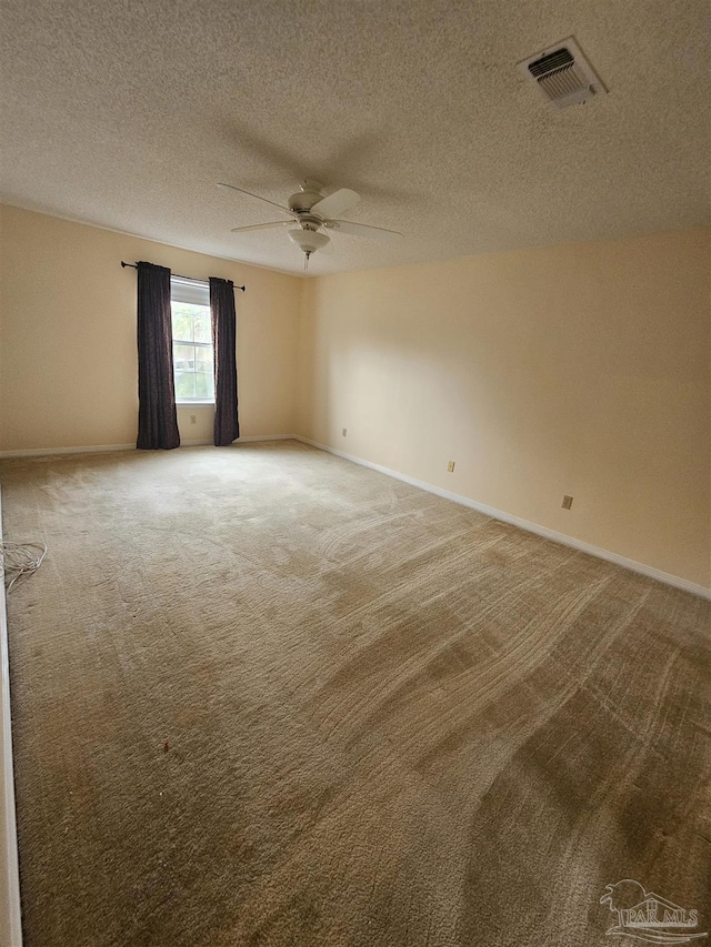 carpeted spare room with a textured ceiling, baseboards, visible vents, and ceiling fan