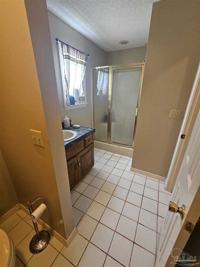 bathroom featuring tile patterned floors, a stall shower, a textured ceiling, baseboards, and vanity