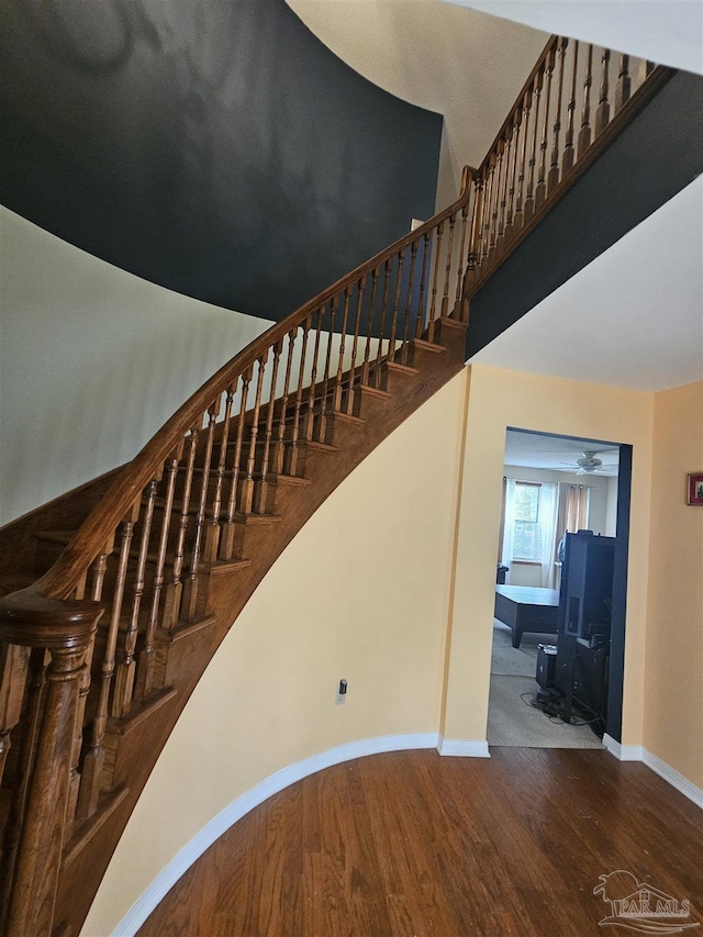 stairway featuring wood finished floors, baseboards, and ceiling fan