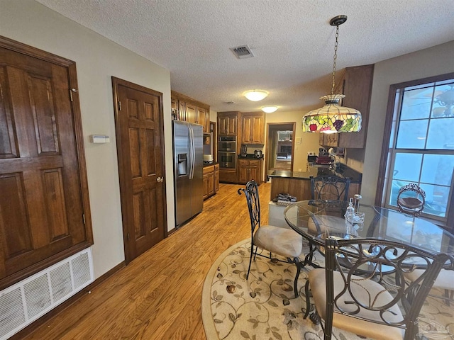 dining room featuring a textured ceiling, baseboards, visible vents, and light wood-type flooring