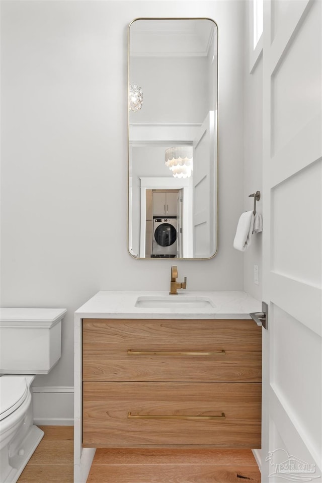 bathroom with toilet, stacked washer / dryer, vanity, wood finished floors, and baseboards