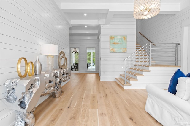 foyer entrance featuring beam ceiling, wooden walls, wood finished floors, a chandelier, and stairs