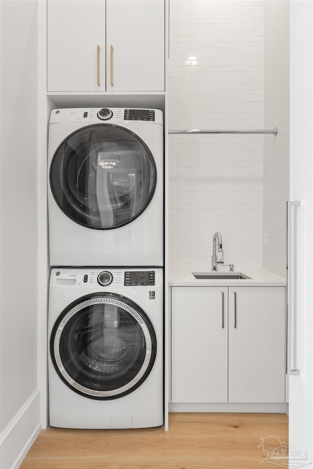 clothes washing area featuring cabinets, stacked washing maching and dryer, sink, and light hardwood / wood-style flooring