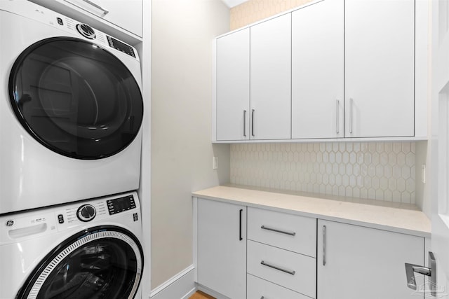 clothes washing area featuring baseboards, cabinet space, and stacked washing maching and dryer