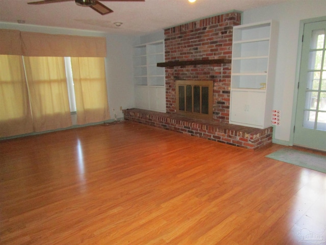 unfurnished living room with ceiling fan, a fireplace, built in features, and wood finished floors