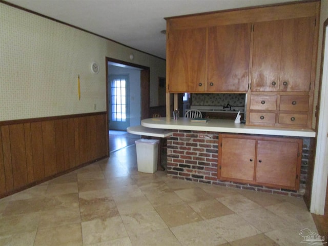 kitchen featuring a wainscoted wall, light countertops, and brown cabinets