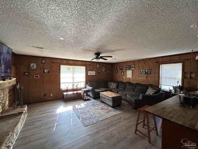 living room featuring wooden walls, ceiling fan, hardwood / wood-style floors, and a textured ceiling