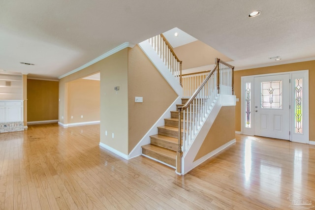 foyer with visible vents, crown molding, light wood-type flooring, stairway, and baseboards