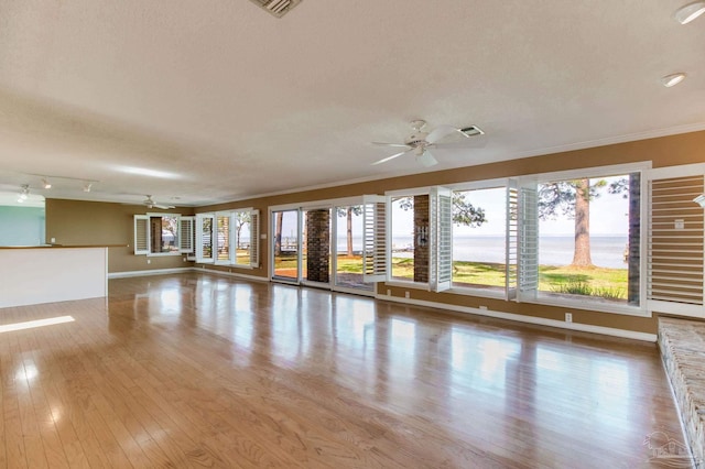 empty room with a ceiling fan, visible vents, crown molding, wood finished floors, and baseboards