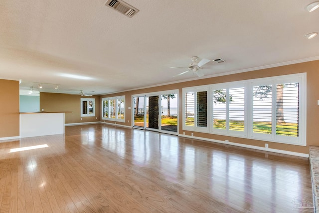 empty room with a ceiling fan, visible vents, wood finished floors, baseboards, and ornamental molding