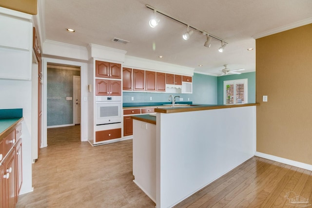 kitchen with ceiling fan, visible vents, white oven, a sink, and ornamental molding
