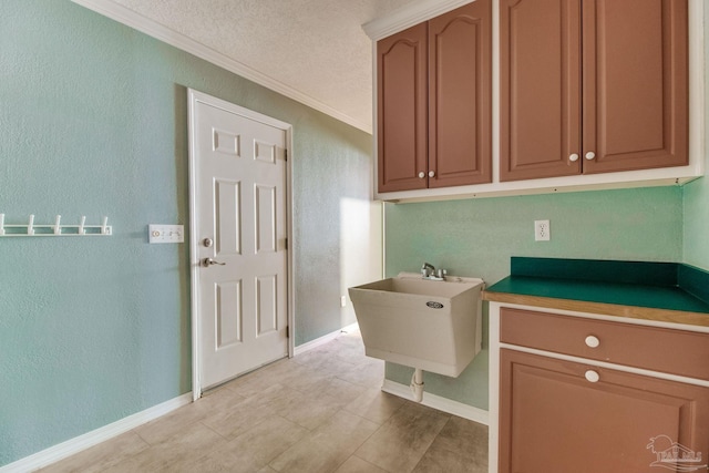 washroom with crown molding, a sink, a textured wall, and baseboards