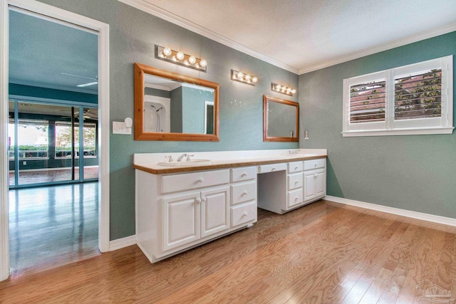 bathroom with double vanity, ornamental molding, wood finished floors, baseboards, and a sink