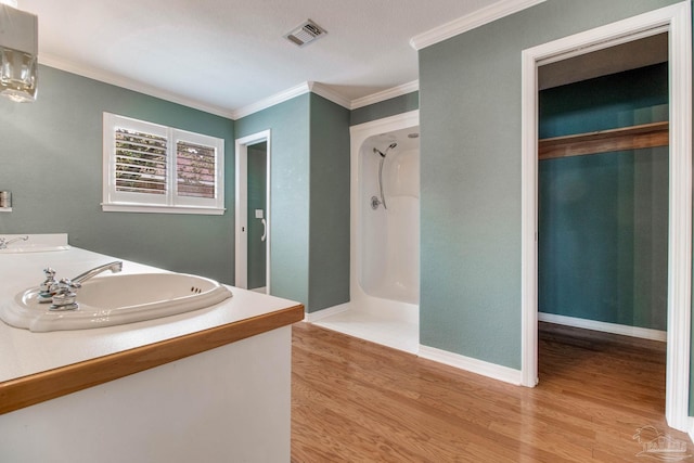 full bathroom featuring visible vents, double vanity, wood finished floors, a walk in shower, and a sink