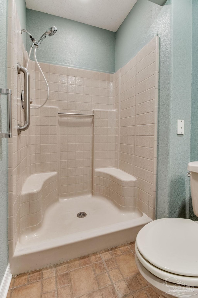 full bathroom featuring toilet, a textured wall, a shower stall, and stone tile flooring