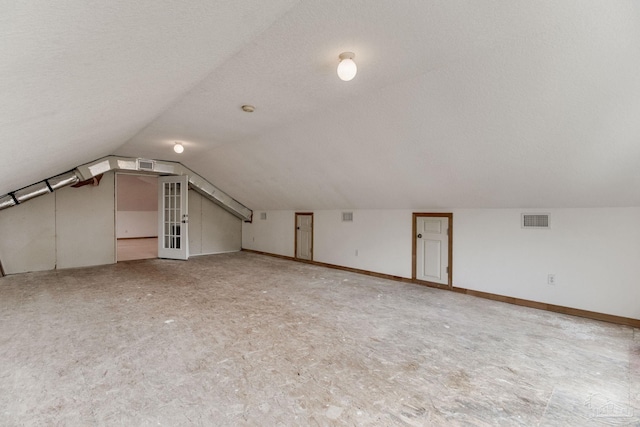additional living space with visible vents, a textured ceiling, and vaulted ceiling