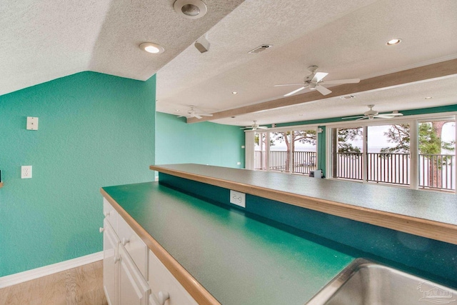 kitchen with a textured wall, baseboards, a textured ceiling, white cabinets, and light wood finished floors