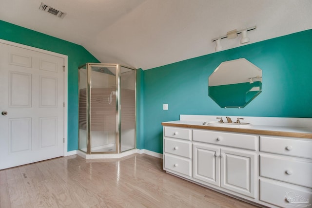 bathroom with vanity, wood finished floors, vaulted ceiling, visible vents, and a stall shower