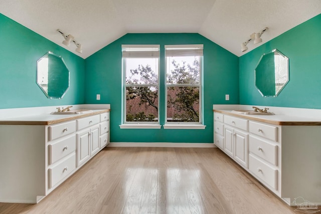 bathroom featuring a sink, rail lighting, two vanities, wood finished floors, and lofted ceiling