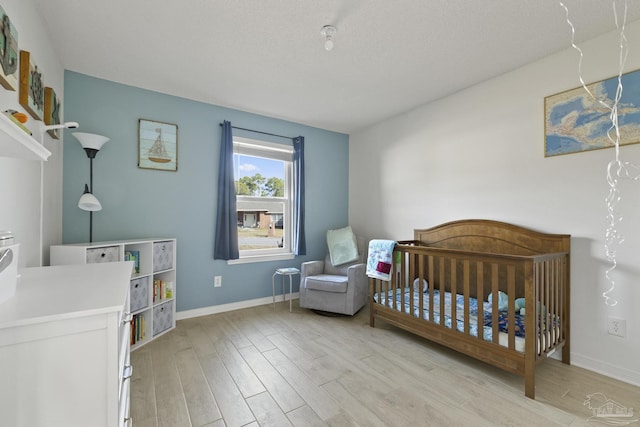 bedroom with a crib, a textured ceiling, and light hardwood / wood-style floors