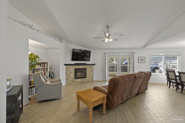 living room featuring vaulted ceiling, a stone fireplace, ceiling fan, and light wood-type flooring