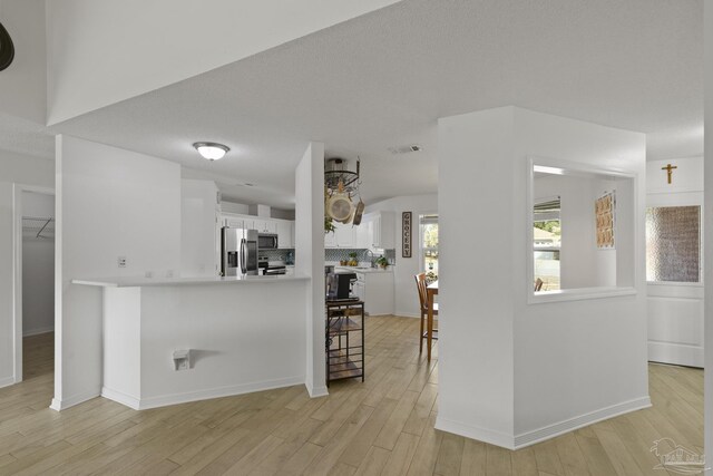 kitchen featuring appliances with stainless steel finishes, tasteful backsplash, white cabinetry, light hardwood / wood-style floors, and kitchen peninsula