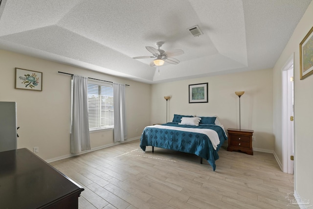 bedroom featuring ceiling fan, a textured ceiling, light hardwood / wood-style floors, and a tray ceiling