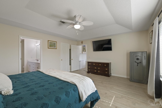 bedroom with connected bathroom, sink, ceiling fan, a raised ceiling, and light hardwood / wood-style flooring