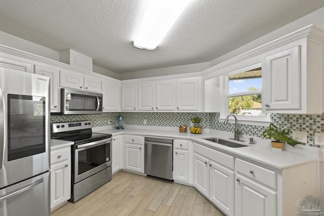 kitchen featuring sink, white cabinetry, light wood-type flooring, stainless steel appliances, and backsplash