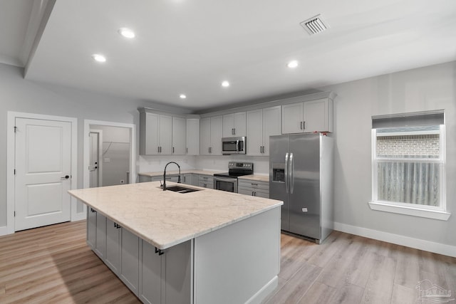 kitchen with sink, light stone counters, light hardwood / wood-style flooring, a kitchen island with sink, and appliances with stainless steel finishes