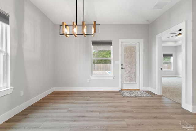 unfurnished dining area featuring ceiling fan with notable chandelier, light hardwood / wood-style flooring, and a wealth of natural light