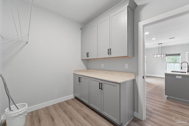 kitchen featuring gray cabinetry, light hardwood / wood-style flooring, pendant lighting, and sink