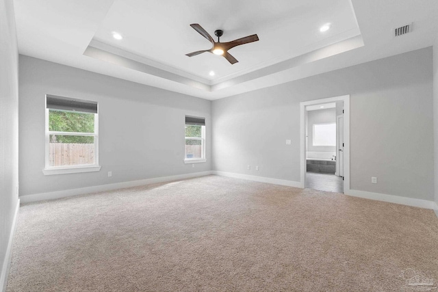 carpeted empty room featuring plenty of natural light, ceiling fan, and a tray ceiling