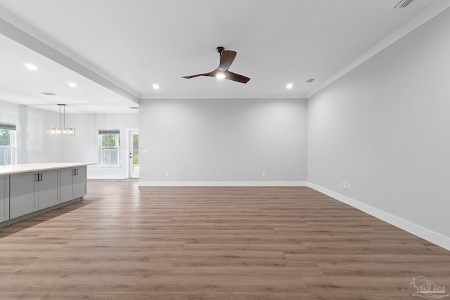 unfurnished living room with ceiling fan with notable chandelier, ornamental molding, and light hardwood / wood-style flooring