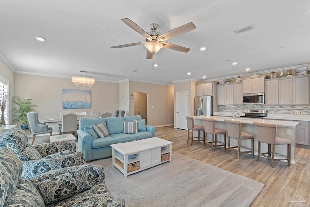 living room with ceiling fan with notable chandelier, light hardwood / wood-style flooring, and crown molding