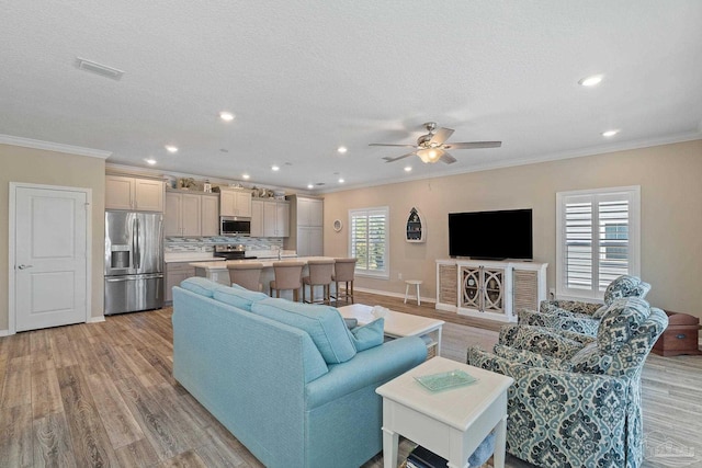 living room featuring a textured ceiling, light wood-type flooring, ceiling fan, and crown molding