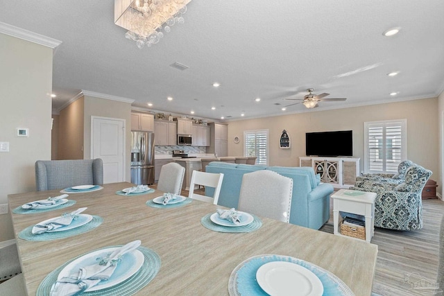 dining space with a textured ceiling, ceiling fan with notable chandelier, light wood-type flooring, and ornamental molding