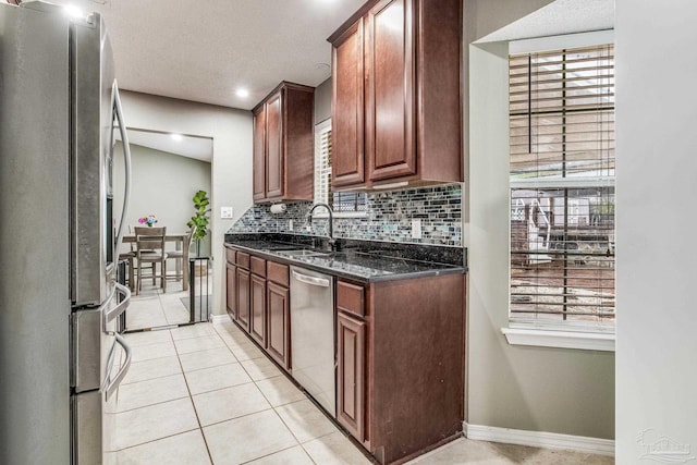 kitchen with light tile patterned floors, stainless steel appliances, tasteful backsplash, dark stone countertops, and sink