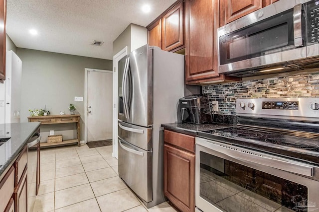 kitchen with a textured ceiling, stainless steel appliances, dark stone countertops, decorative backsplash, and light tile patterned flooring