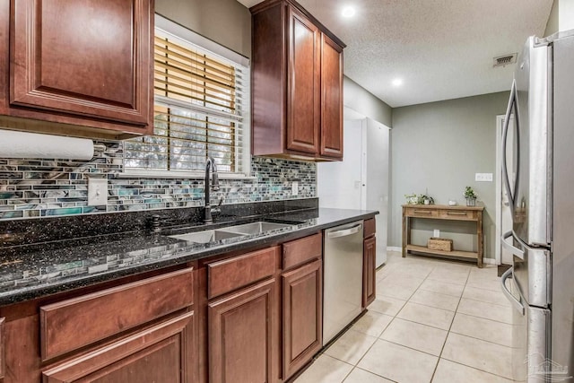 kitchen with light tile patterned floors, stainless steel appliances, dark stone counters, a textured ceiling, and sink