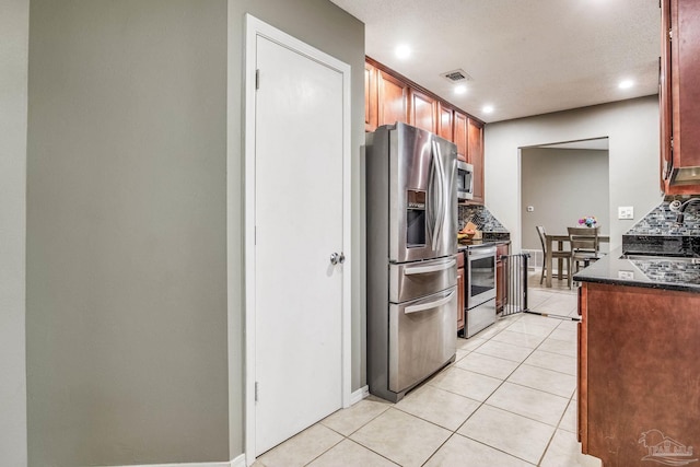 kitchen with light tile patterned floors, stainless steel appliances, decorative backsplash, dark stone countertops, and sink