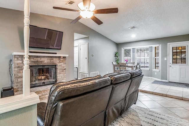 living room with lofted ceiling, ceiling fan, a fireplace, light tile patterned flooring, and a textured ceiling