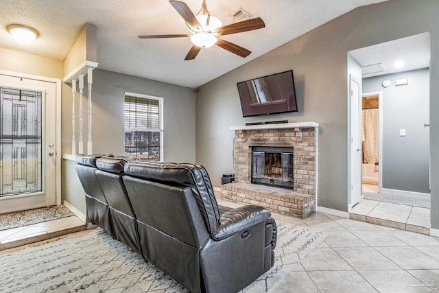 tiled living room with ceiling fan, vaulted ceiling, a brick fireplace, and a textured ceiling