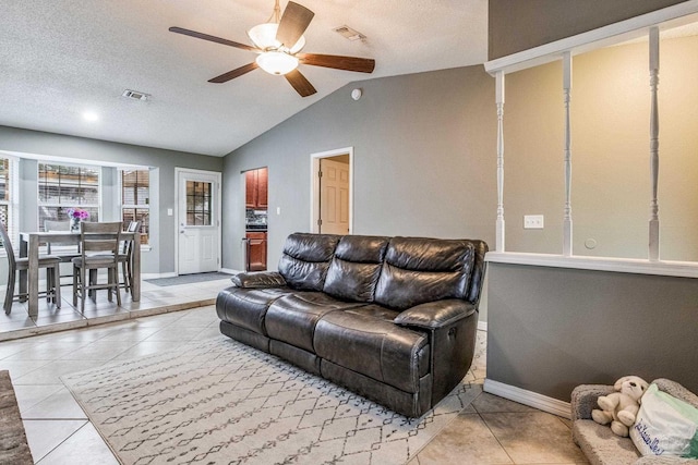 living room with ceiling fan, a textured ceiling, vaulted ceiling, and light tile patterned flooring