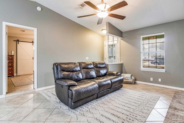 tiled living room featuring vaulted ceiling, ceiling fan, a textured ceiling, and a barn door