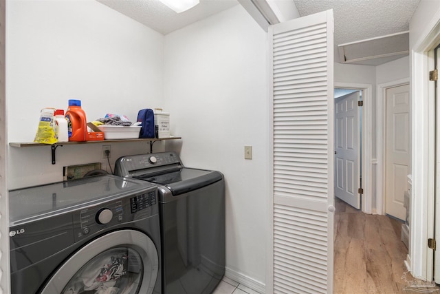 washroom featuring a textured ceiling, washer and clothes dryer, and light hardwood / wood-style flooring