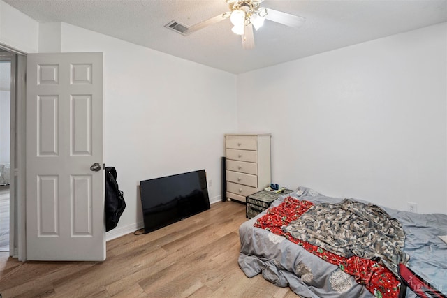 bedroom with a textured ceiling, ceiling fan, and light wood-type flooring